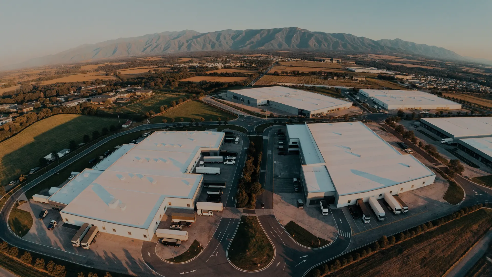 Vista aérea de un parque industrial moderno al atardecer, con naves y accesos